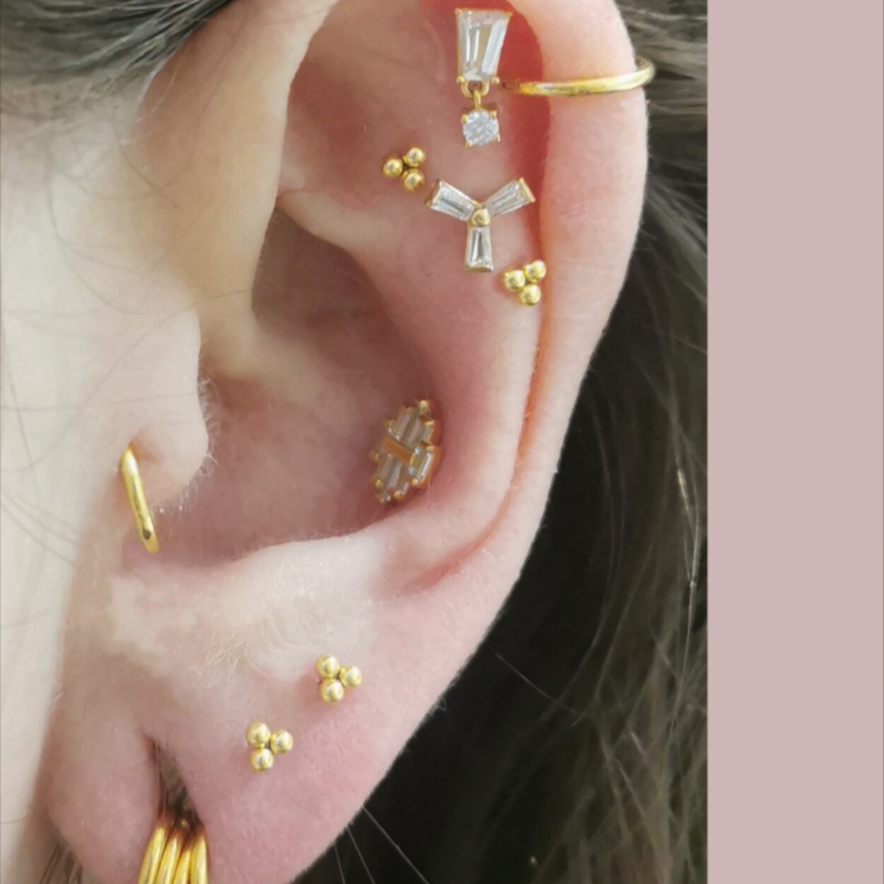 Schmuckstyling von Miri. Goldener Titanschmuck mit kristallenen Elementen in Flat-, Conch-, Helix-, Lobe-, Tragus-Piercing bei Fine Line Berlin. Dieser ästhetisch goldene Titanschmuck mit unterschiedlichen kristallenen Elementen wurde in jeweils Flat-, Conch-, Helix-, Lobe- und Tragus-Piercings eingesetzt.